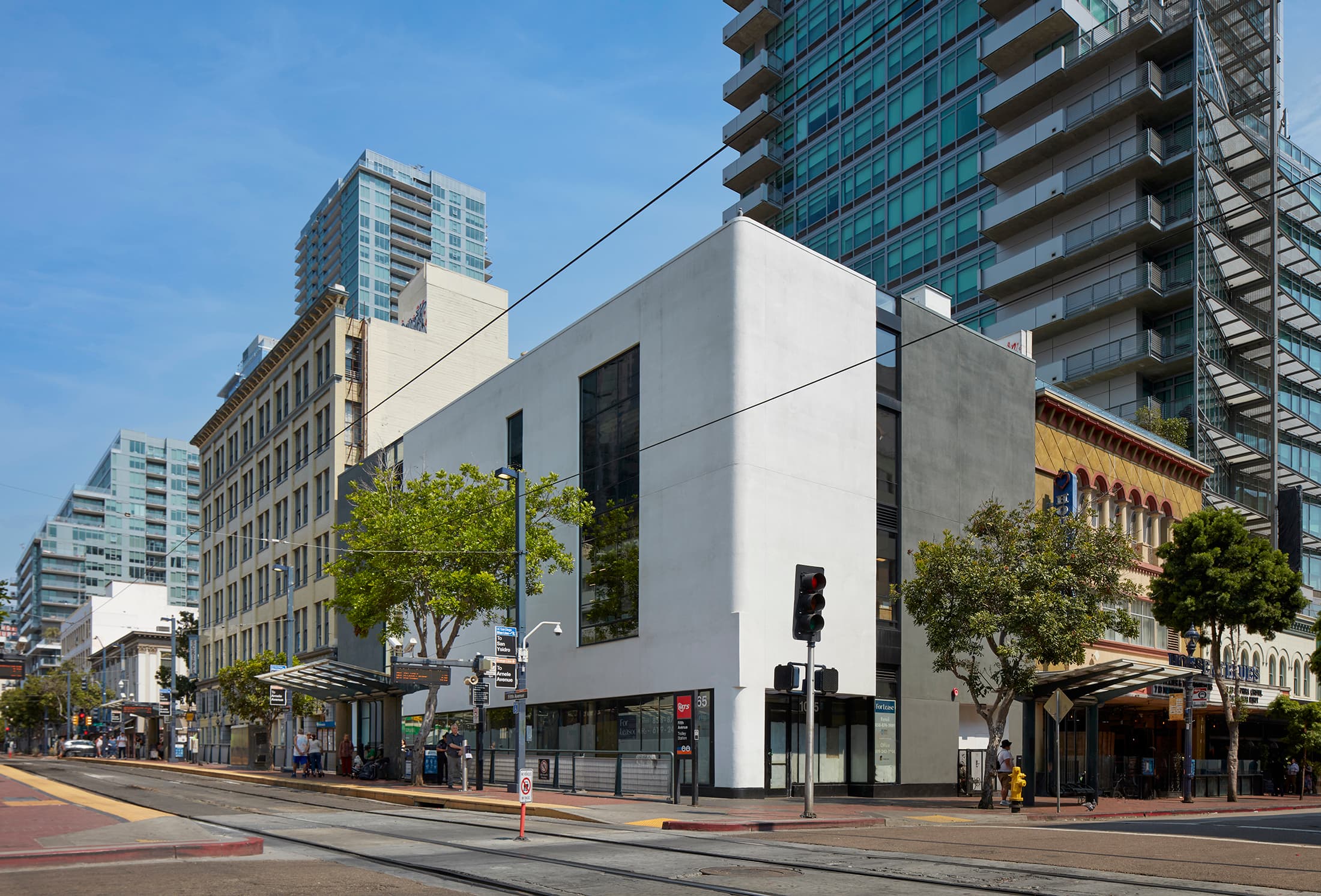 5th & C in downtown San Diego, a renovated white three-storey corner building beside the Fifth Avenue trolley stop with glass towers behind it