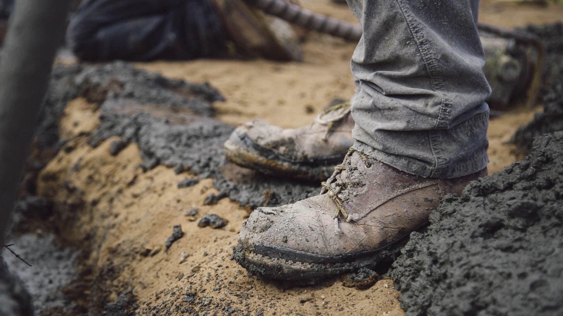 A mud-caked work boot planted on a fresh concrete pour