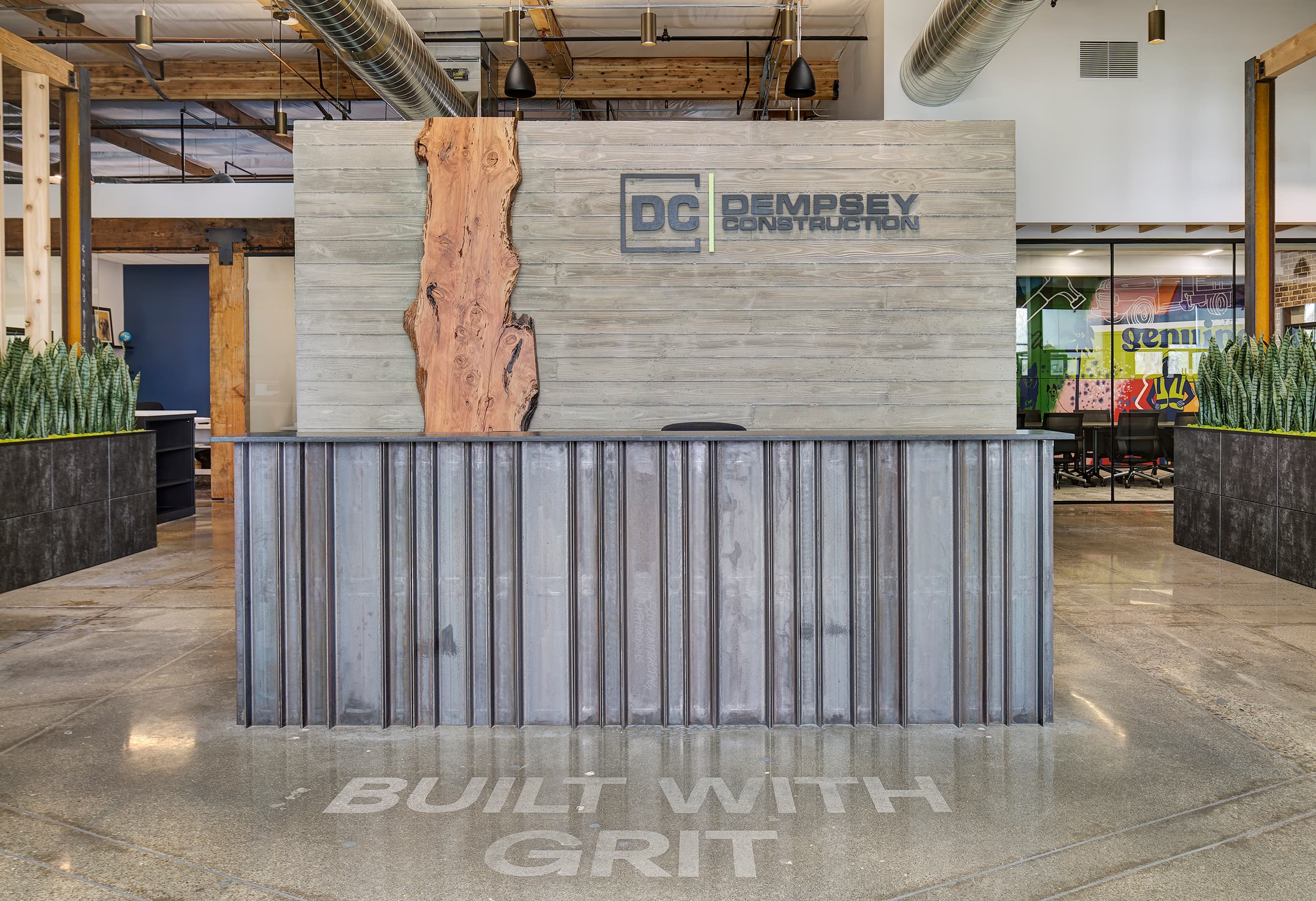 The Dempsey office lobby, a live-edge timber reception desk under the logo and the words Built With Grit set into the concrete floor