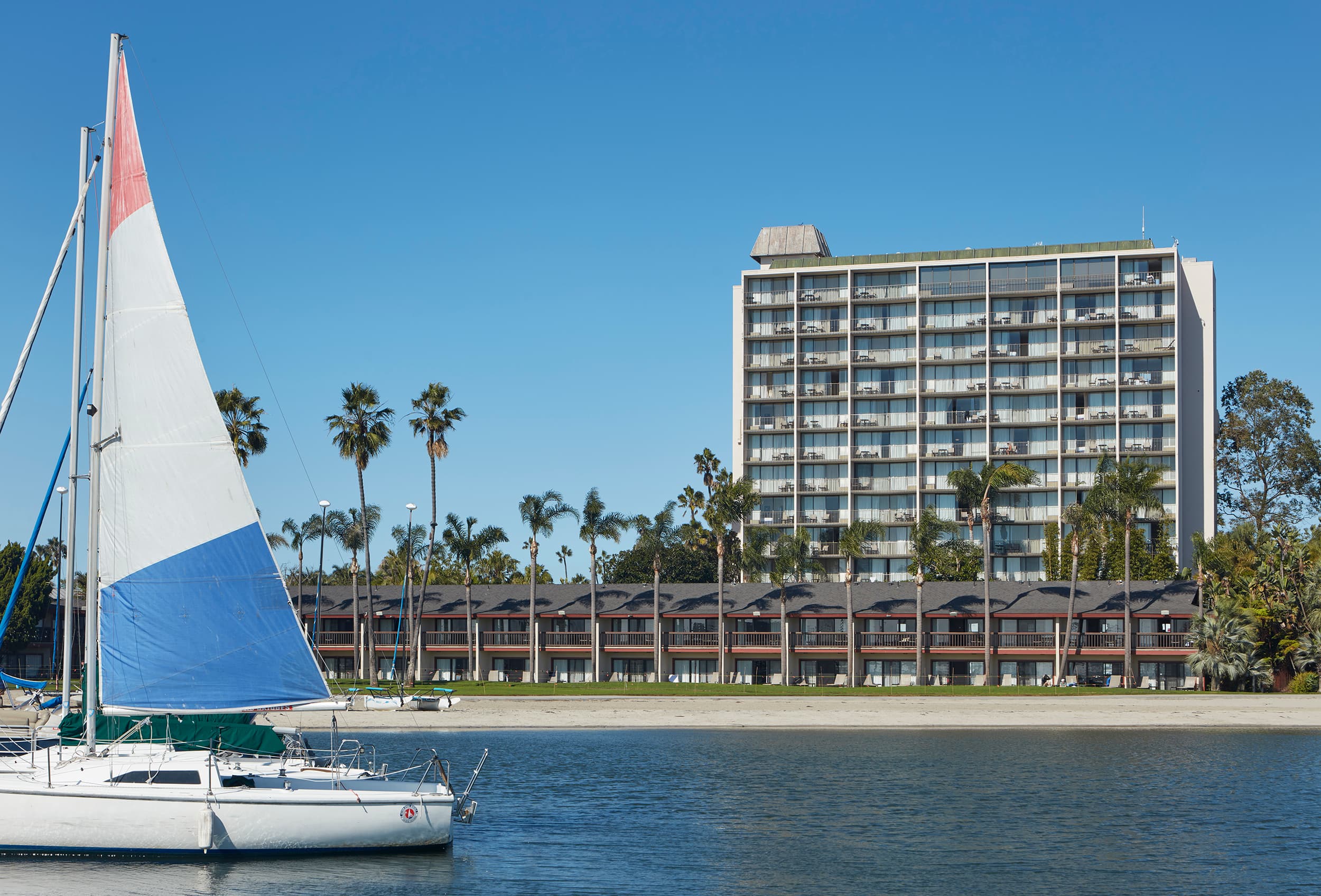 Catamaran Hotel on Mission Bay in San Diego, a tower above palm trees with a sailboat passing in the foreground