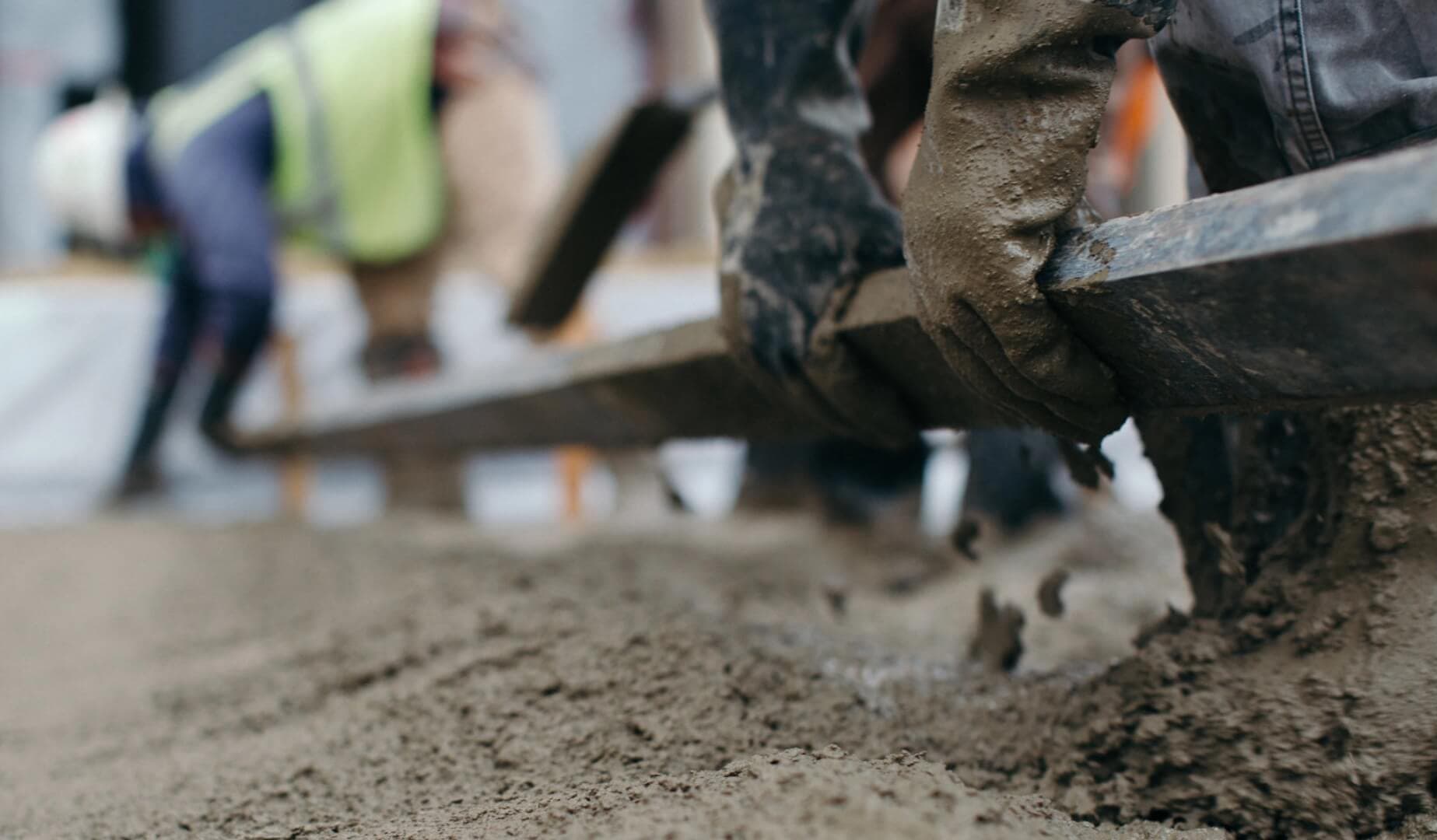 Gloved hands dragging a screed across a fresh concrete pour, the crew blurred behind