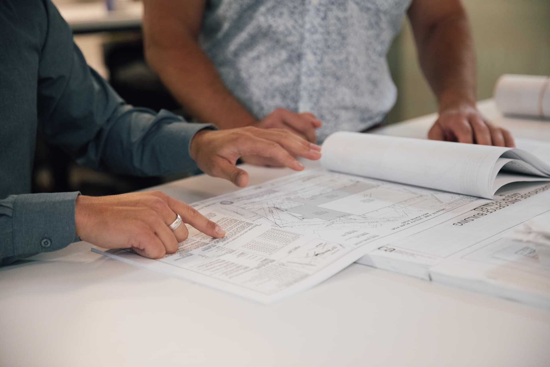 Three people at a table reviewing a set of construction drawings, one pointing at a detail