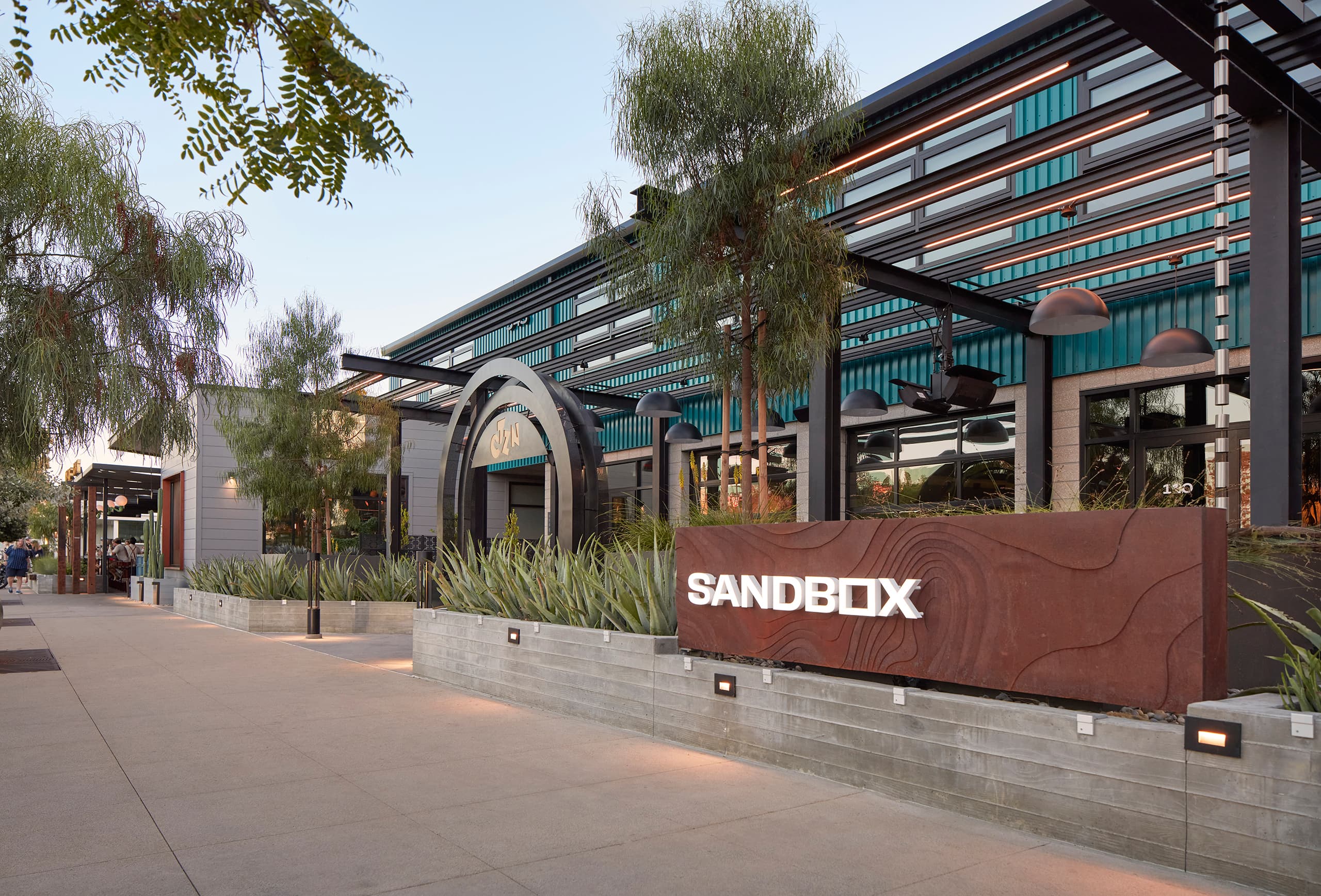 The Sandbox in Solana Beach, a modern mixed-use campus with the Sandbox sign on a low concrete wall and a glass-and-steel building behind it