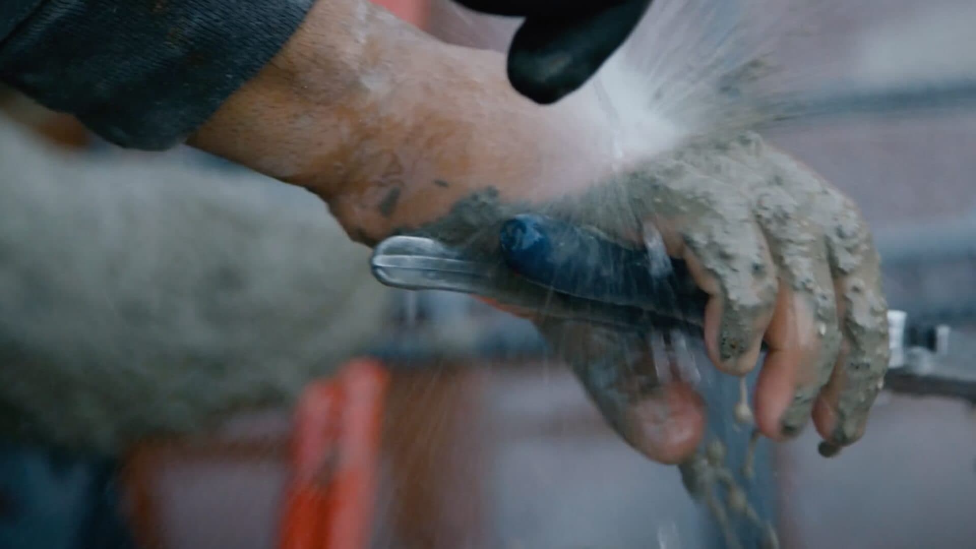 Gloved hands drawing a trowel through wet concrete