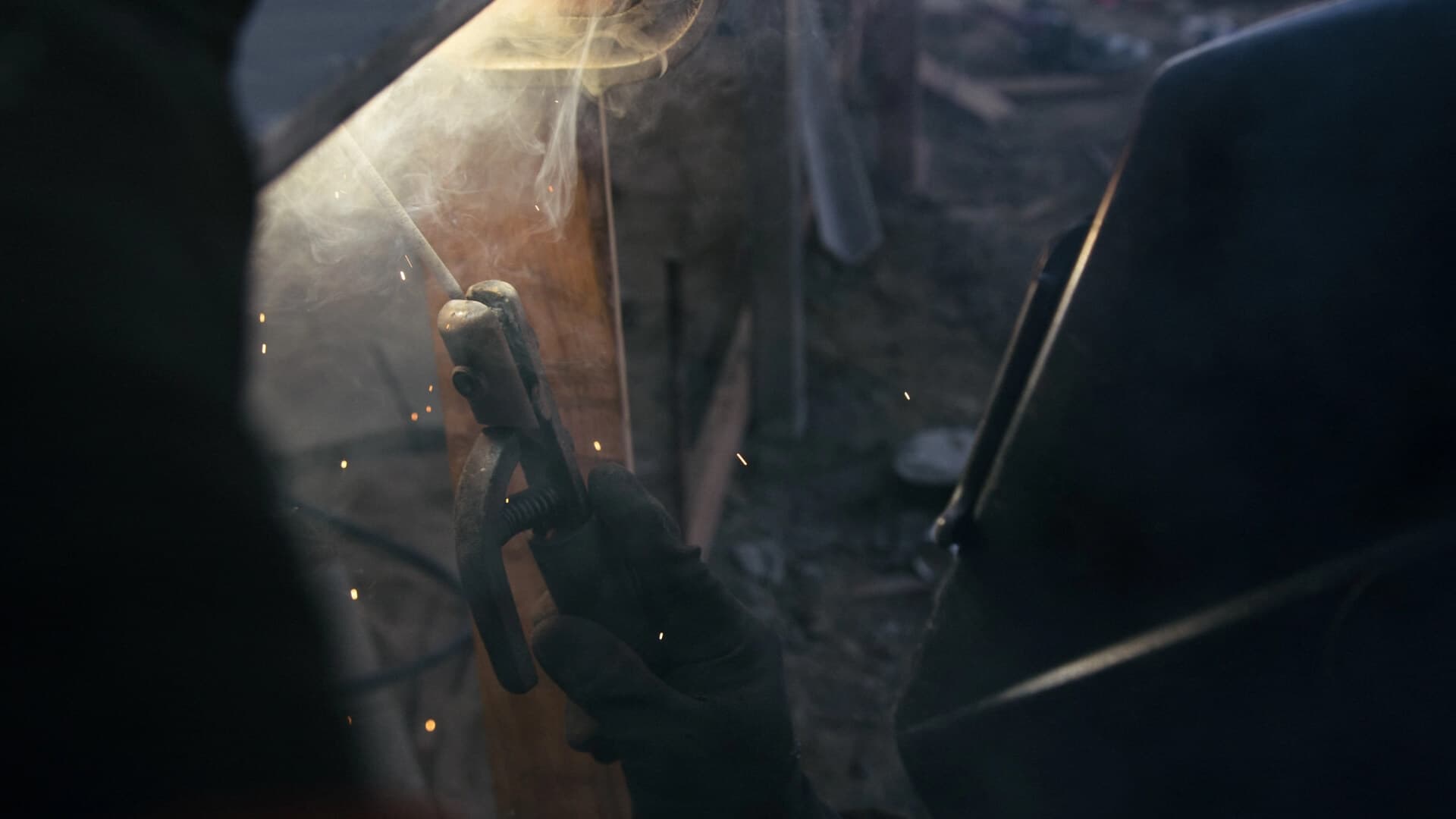 A welder at work in low light, sparks flying from the joint