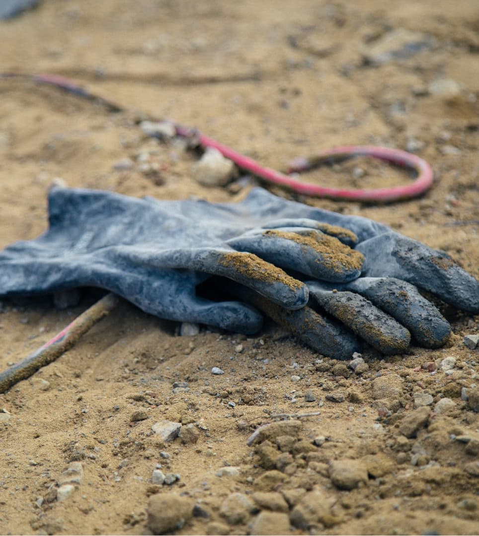 A pair of worn work gloves and a coiled air hose on bare earth
